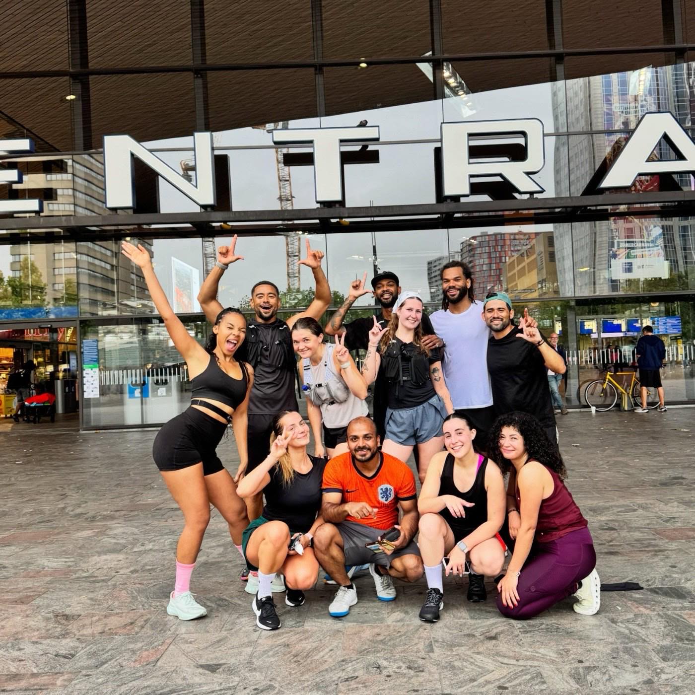 The LEVELS Run Club crew outside Rotterdam Centraal after a Sunday 5K, throwing up the L sign